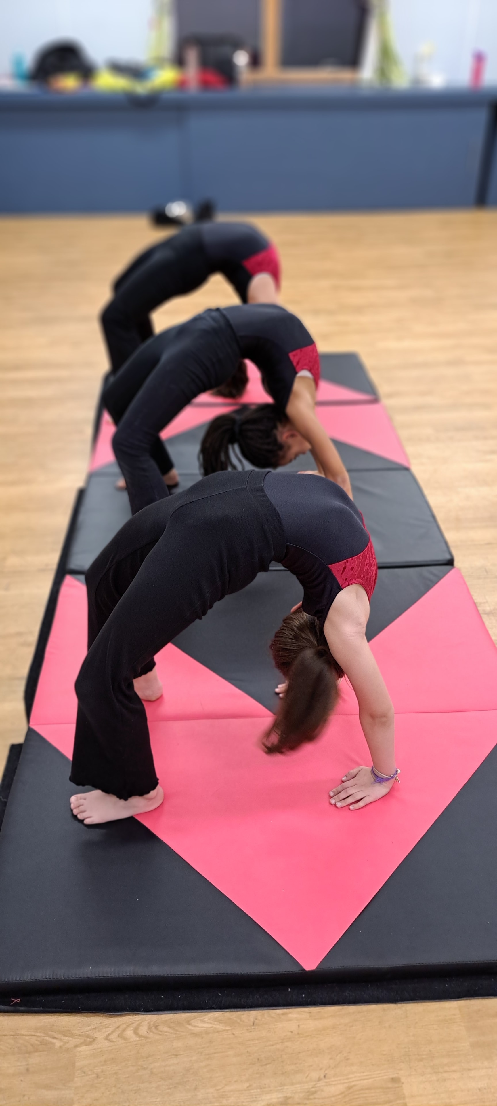 Three students performing back bends on pink mats